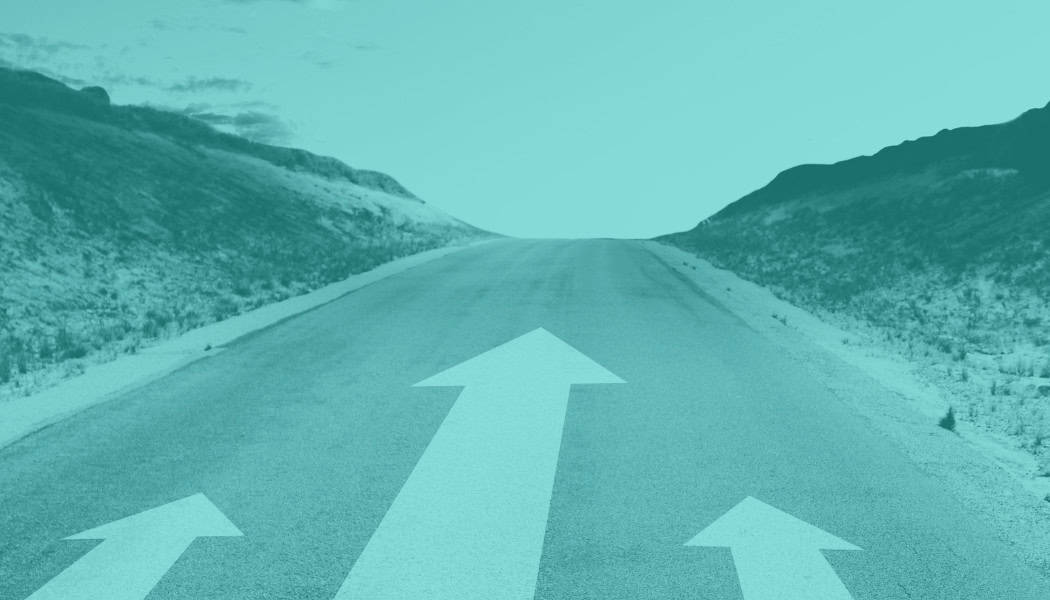 road with three forward arrows painted on the road surface. Rough hilly terrain on either side of the road