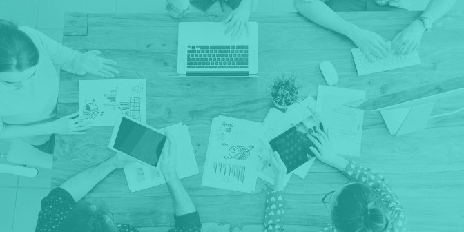 View from above a desk with laptop, papers and people sat around it
