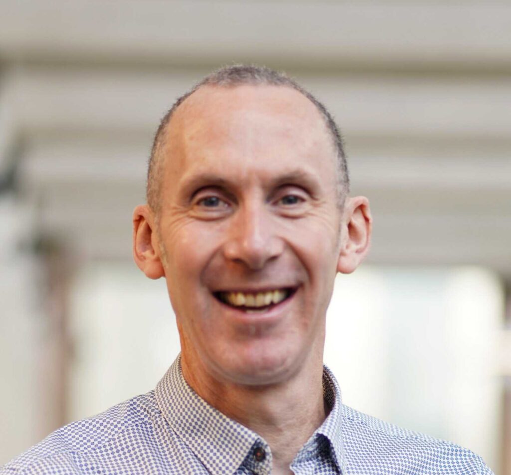 Headshot of Robin smiling and facing the camera wearing a checked shirt